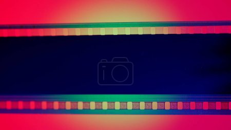 Photo for Black strip of film on red background with green circular light close up. Cinema filmstrip on red background. 35mm film slide frame. Cinema or photo frames. Long, retro film strip frame. Copy space - Royalty Free Image