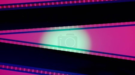 Foto de Dos tiras de película negra sobre fondo rosa iluminadas con luz circular verde, de cerca. Copiar espacio - Imagen libre de derechos