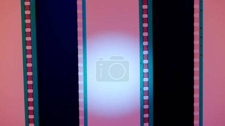 Téléchargez les photos : Deux bandes de film verticales sur fond rose avec lumière circulaire blanche, fermer. Cadre de diapositive de film 35mm. Long, cadre de bande de film rétro. Espace de copie - en image libre de droit