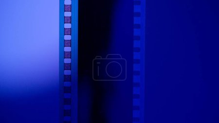 Foto de Franja vertical de película en blanco sobre fondo azul degradado de cerca. Procesando negativos. Copiar espacio - Imagen libre de derechos