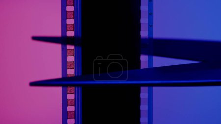 Foto de Tijeras corta una tira de película fotográfica sobre un fondo azul y rosa de cerca - Imagen libre de derechos