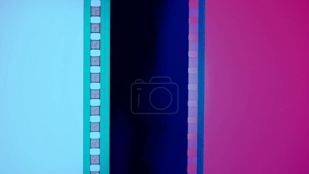 Foto de Tiras verticales de película sobre fondo azul y rosa, de cerca. Marco de diapositiva de película de 35 mm. Marco de tira de película largo y retro. Copiar espacio - Imagen libre de derechos