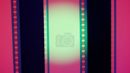 Foto de Dos tiras verticales de película sobre un fondo rojo con luz circular verde, de cerca. Marco de diapositiva de película de 35 mm. Marco de tira de película largo y retro. Copiar espacio - Imagen libre de derechos
