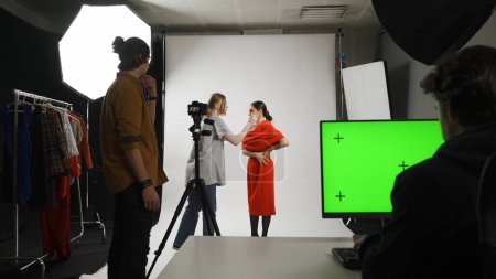 Photo for Photo production and creative teamwork concept. Backstage of model and professional team in the studio. Stylist assistant fixing look of model on set, editor at the desktop chroma key green screen. - Royalty Free Image