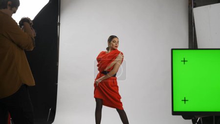 Photo for Photo production and creative teamwork concept. Backstage of model and professional team in the studio. Female model posing for photographer, editor table at the side chroma key green screen. - Royalty Free Image