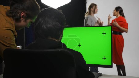 Photo for Photo production and creative teamwork concept. Backstage of model and professional team in the studio. Editor and photographer looking at monitor checking pictures, chroma key green screen. - Royalty Free Image