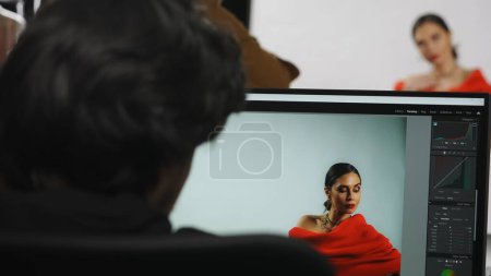 Photo for Photo production and creative teamwork concept. Backstage of model and professional team in the studio. Model posing on set, male editor working on computer looking at photos on monitor. - Royalty Free Image