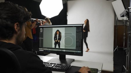 Photo for Photo production and creative teamwork concept. Backstage of model and professional team in the studio. Shot of male editor at monitor chroma key green screen, model and assistant stylist at the back. - Royalty Free Image