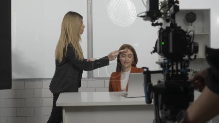 Photo for Crew preparing for shoot in studio. The videographer mounts the camera on a tripod, the make up woman applies the make up of the TV presenter - Royalty Free Image