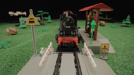 Téléchargez les photos : Un modèle de train à vapeur en plastique pour enfants debout sur une plate-forme au milieu d'un paysage verdoyant. Atmosphère parfaite pour une utilisation dans les présentations d'enfants ou la publicité de jouets - en image libre de droit