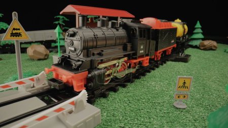 Téléchargez les photos : Modèle d'un train à vapeur en plastique pour enfants avec des wagons de marchandises debout sur une plate-forme au milieu d'un paysage verdoyant. Atmosphère parfaite pour une utilisation dans les présentations d'enfants ou la publicité de jouets - en image libre de droit