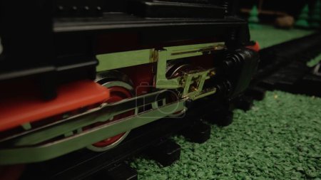 Téléchargez les photos : Un modèle de train en plastique pour enfants voyageant le long des voies ferrées au milieu d'un paysage verdoyant. Gros plan des roues. Atmosphère idéale pour une utilisation dans les présentations pour enfants ou dans la publicité pour jouets - en image libre de droit