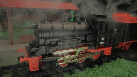 Téléchargez les photos : Enfants train à vapeur jouet en fumée. Gros plan de la locomotive modèle avec vapeur. Atmosphère idéale pour une utilisation dans les présentations pour enfants ou dans la publicité pour jouets - en image libre de droit