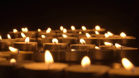 Téléchargez les photos : Des rangées de bougies allumées. Les bougies brûlent sur un fond noir. Le concept d'une journée commémorative. Contexte des projets de publicité et de design - en image libre de droit