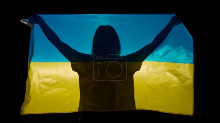 Photo for National flags patriotic advertisement concept. Person silhouette holding big flag against black background. Silhouette of woman with national flag of Ukraine holding in hands. - Royalty Free Image