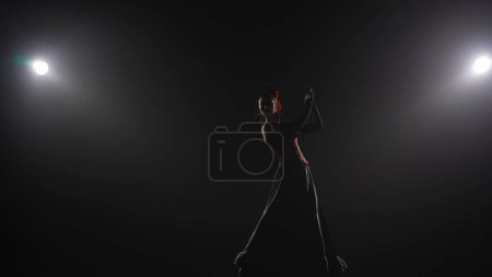 Modern choreography an dance. Woman dancing on black background under spotlights. Spanish dancer in red-black dress dancing elements of passionate flamenco.