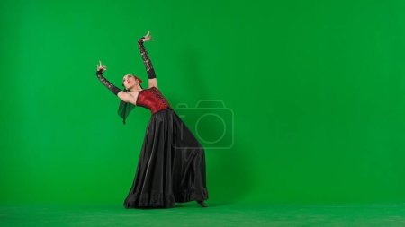 Photo for Modern choreography an dance. Woman dancer dancing on chroma key green screen. Female in flamenco style dress performs elegant spanish dance moves with her hands and body in the studio. - Royalty Free Image