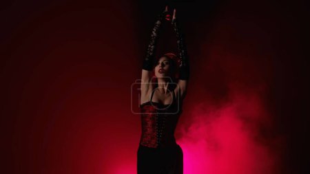 Foto de Coreografía moderna un baile. Mujer bailando sobre fondo negro con luz roja y humo. Bailarina española en traje rojo y negro demuestra elementos de coreografía flamenca. - Imagen libre de derechos