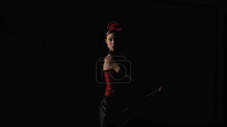 Foto de Coreografía moderna un baile. Mujer bailando sobre fondo negro bajo focos. Bailarina española en traje rojo-negro elementos de baile de flamenco apasionado. - Imagen libre de derechos