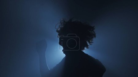 Foto de Silueta en concepto de iluminación. Modelo masculino contra luz brillante sobre fondo negro en estudio. Hombre clubber silueta bailando rodeado de rayos de luz en la oscuridad. - Imagen libre de derechos