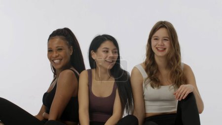 Téléchargez les photos : Portrait de jeunes modèles multiethniques isolés sur fond de studio blanc. Groupe de trois filles multiraciales positives assis posant en souriant à la caméra Concept de beauté multiethnique - en image libre de droit