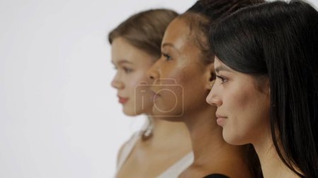 Foto de Retrato de jóvenes modelos multiétnicos sobre fondo blanco de cerca. Grupo de tres atractivas chicas multirraciales de pie mirando hacia otro lado de la cámara. Concepto de belleza multiétnica - Imagen libre de derechos