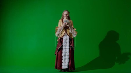 Photo for Historical person modern lifestyle advertisement. Woman in ancient outfit on the chroma key green screen background. Woman in renaissance style dress holding a fan of money and very happy. - Royalty Free Image