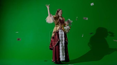 Persona histórica estilo de vida moderno anuncio. Mujer en traje antiguo en el fondo de pantalla verde croma clave. Mujer en vestido de estilo renacentista lanza billetes en el aire.