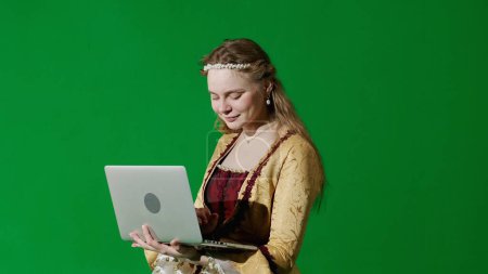 Photo for Historical person modern lifestyle advertisement. Woman in ancient outfit on chroma key green screen background. Female in renaissance style dress holding laptop typing message. - Royalty Free Image
