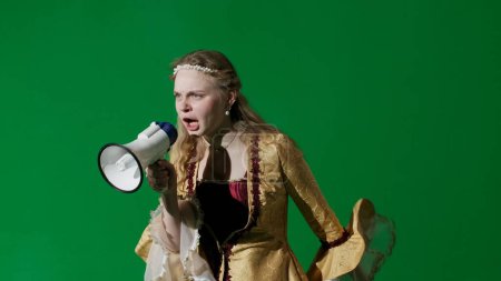 Photo for Historical person modern lifestyle advertisement. Woman in ancient outfit on the chroma key green screen background. Woman in renaissance dress holding megaphone and angrily shouting slogans at a - Royalty Free Image