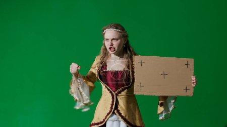 Photo for Historical person modern lifestyle advertisement. Woman in ancient outfit on chroma key green screen background. Woman in renaissance dress holding cardboard sign and shouting slogan at protest. - Royalty Free Image