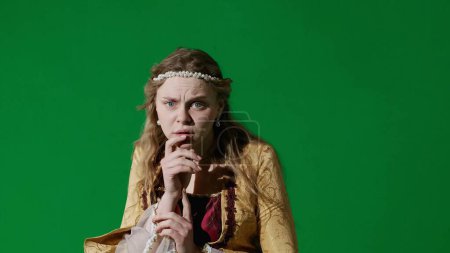 Photo for Historical person modern lifestyle advertisement. Woman in ancient outfit on chroma key green screen background. Female in renaissance style dress posing looking at the camera, scared shocked face. - Royalty Free Image