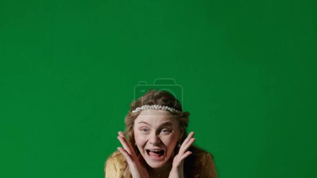 Photo for Historical person modern lifestyle advertisement. Woman in ancient outfit on the chroma key green screen background. Female in renaissance style dress looking at the camera, amazed surprised face. - Royalty Free Image