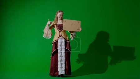 Photo for Historical person modern lifestyle advertisement. Woman in ancient outfit on chroma key green screen background. Female in renaissance style dress holding cardboard sign talking advertising service - Royalty Free Image