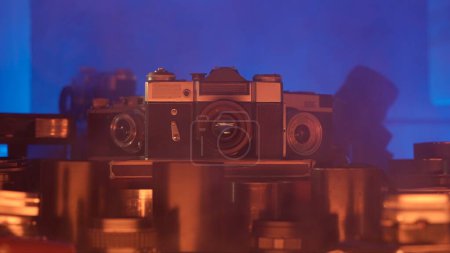 Photo for Vintage collection of antique cameras and lenses. Immerse yourself in an atmosphere of mystery and magic with this video where vintage cameras and lenses are enveloped in neon light and smoke - Royalty Free Image