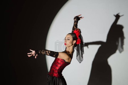Photo for Modern choreography an dance. Woman dancing on black background under spotlights. Spanish dancer in red-black dress dancing elements of passionate flamenco. - Royalty Free Image