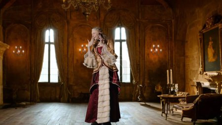 Photo for Historical person modern lifestyle advertisement. Woman in ancient outfit on background of historic interior. Female in renaissance style dress calling talking on smartphone. - Royalty Free Image