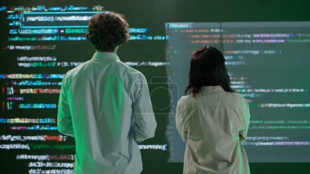 Photo for Futuristic university and artificial intelligence concept. IT specialists against big digital screen. Back view of woman and man engineers stand in front of screen with digital code data error process - Royalty Free Image