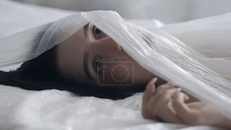 Photo for Body beauty and fashion advertisement. Close up of womans face and eyes partially covered by translucent oilcloth - Royalty Free Image