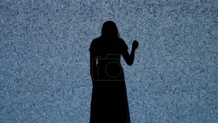 Photo for Halloween horror movie creative concept. Silhouette against digital television screen. Thriller scene scared woman with knife walks back in front of big digital screen with white noise. - Royalty Free Image