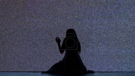 Photo for Halloween horror movie creative concept. Silhouette against digital television screen. Thriller scene scared trapped woman silhouette sitting on the floor hitting big digital screen with noise. - Royalty Free Image