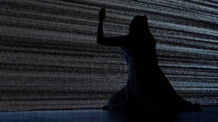 Kreatives Konzept für den Horrorfilm zu Halloween. Silhouette gegen digitalen Fernsehbildschirm. Thriller-Szene verängstigt gefangene Frau Silhouette sitzt auf dem Boden und schlägt große digitale Leinwand mit Lärm.