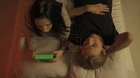 Photo for Love intimate relationships concept. Top view loving couple romantic time in bedroom. Man and woman sensual lovers laying in bed together, talk smiling, female with smartphone chroma key green screen. - Royalty Free Image