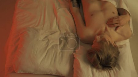 Foto de Vista superior de un hombre joven semidesnudo acostado en una cama en un dormitorio. Varón con torso desnudo. Concepto de romance, amor, relación - Imagen libre de derechos