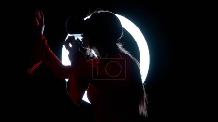 Photo for Digital visual technology concept. Woman silhouette in virtual reality glasses standing in front of digital screen wall with neon symbols looking around playing video game. - Royalty Free Image