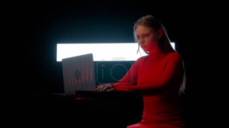 Téléchargez les photos : Concept de technologie visuelle numérique. Jeune femme avec ordinateur portable contre le mur numérique dans le club sombre. Silhouette de femme assise tapant sur l'ordinateur portable, jouant mélangeant la musique devant le grand écran numérique. - en image libre de droit