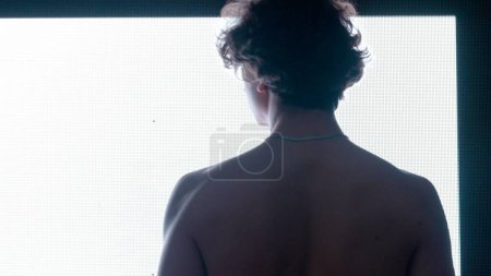 Téléchargez les photos : Concept de technologie visuelle numérique. Homme avec torse nu contre un mur numérique noir. Silhouette rapprochée d'un homme debout devant un écran numérique avec des symboles abstraits, vue arrière - en image libre de droit