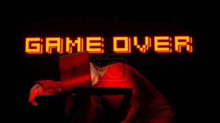 Photo for Digital visual technology concept. Young female napping at the table with laptop in dark club. Woman silhouette gamer sleeping with open laptop and sign text game over behind. - Royalty Free Image