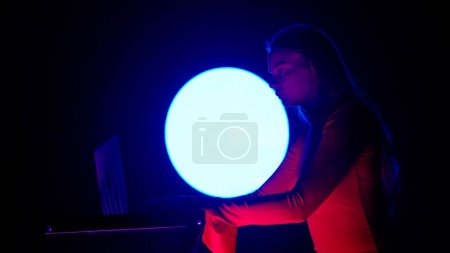 Photo for Digital visual technology concept. Young female with laptop against digital wall in dark club. Woman silhouette sitting typing on laptop, gaming mixing music, neon symbols digital screen. - Royalty Free Image