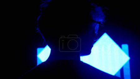 Photo for Digital visual technology concept. Male silhouette close up against digital wall in dark club. Man standing looking towards big digital screen background with neon symbols, back shot. - Royalty Free Image
